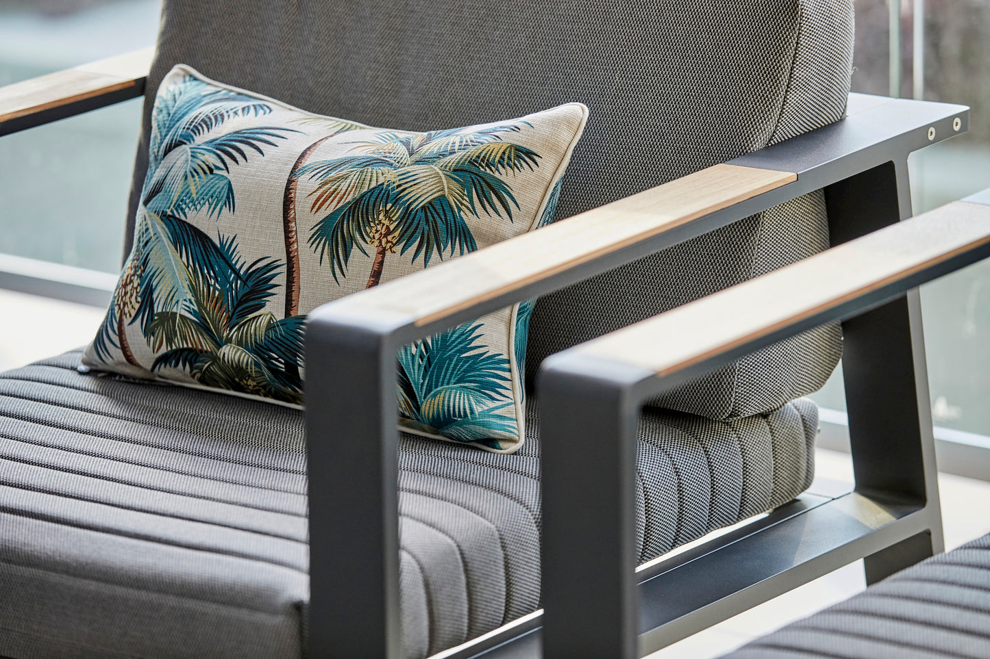 Gray outdoor sofa with a decorative pillow featuring palm trees on a patio.