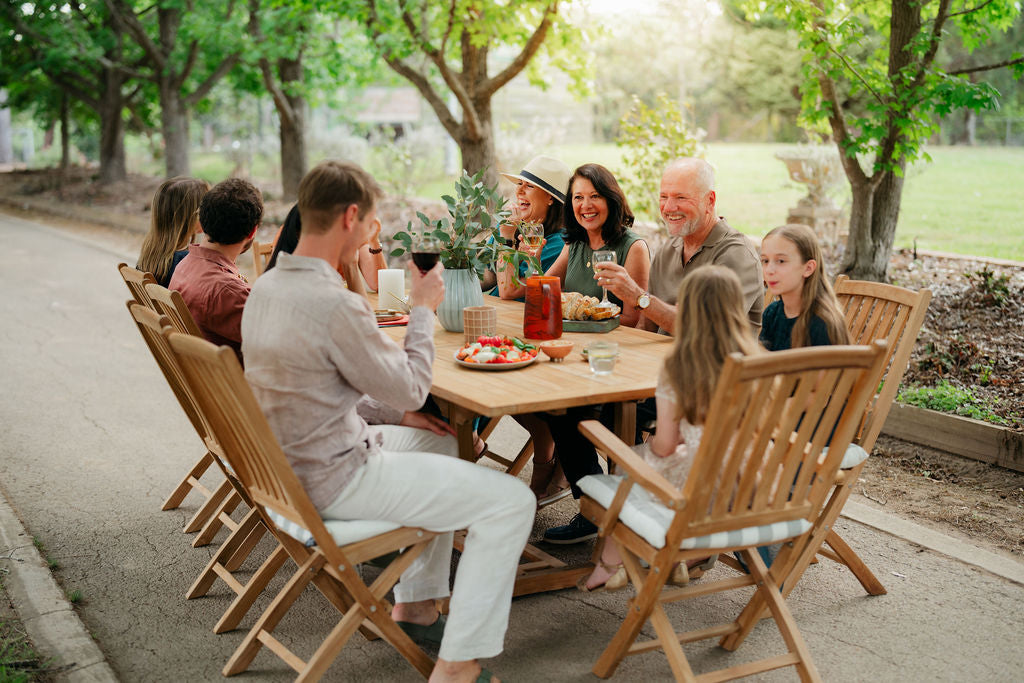 Family enjoying a meal outdoors at a wooden table with chairs.