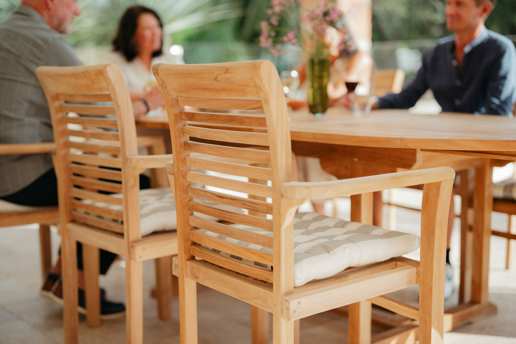 Wooden chairs with cushions at an outdoor dining table, blurred people in the background