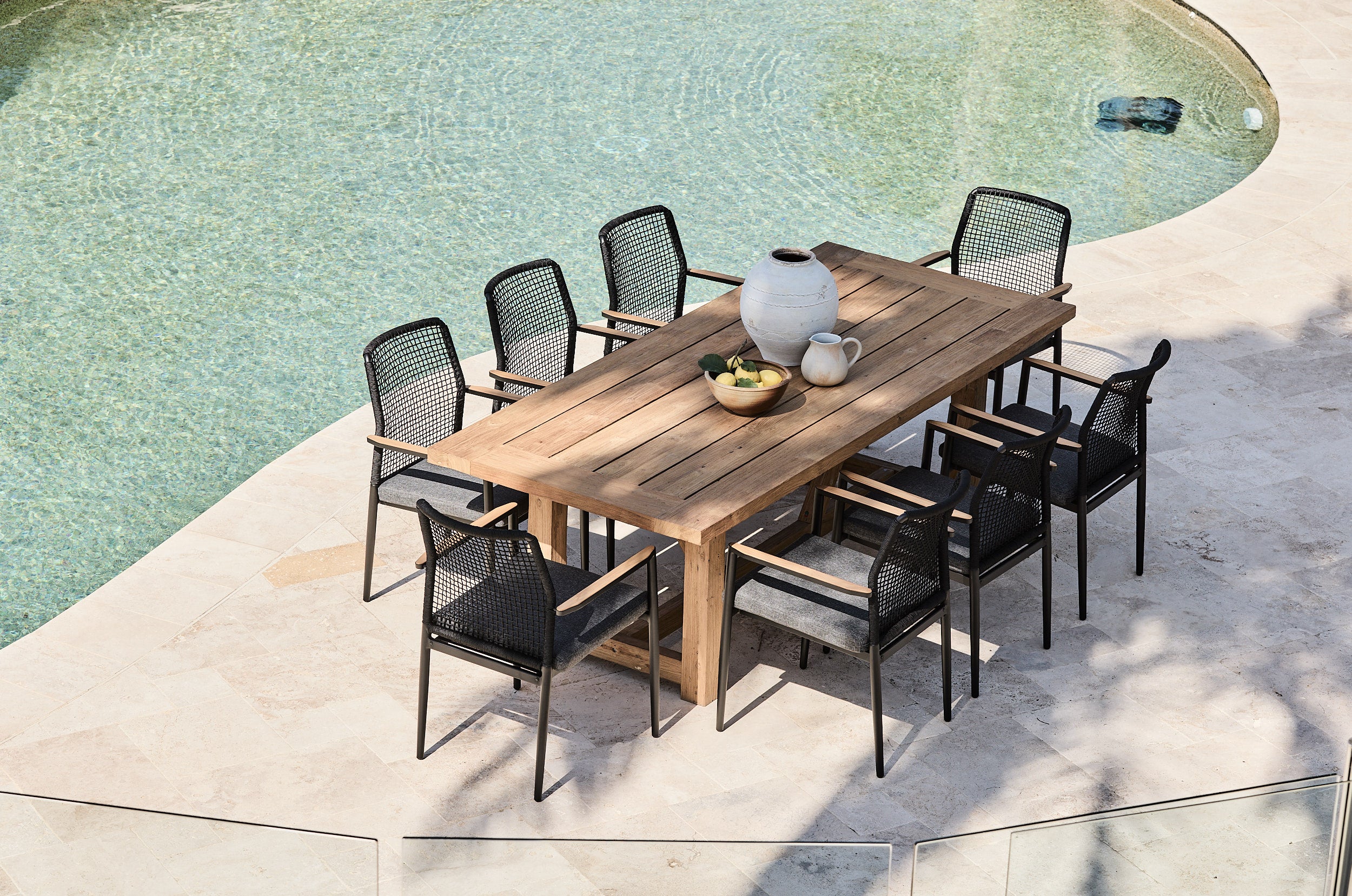 Outdoor dining set with a wooden table and black chairs by a pool.
